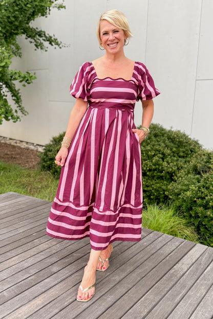 Front view of woman wearing Swagger Boutique’s Plum &amp; Pink Striped Midi Dress by Entro with sandals standing outside on a deck.