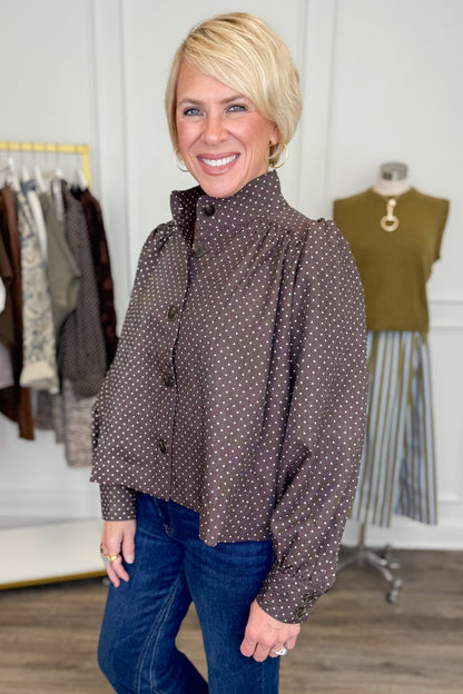 Side view of woman wearing Swagger Boutique’s Polka Dot Button Up Top with jeans with clothing hanging in the background.