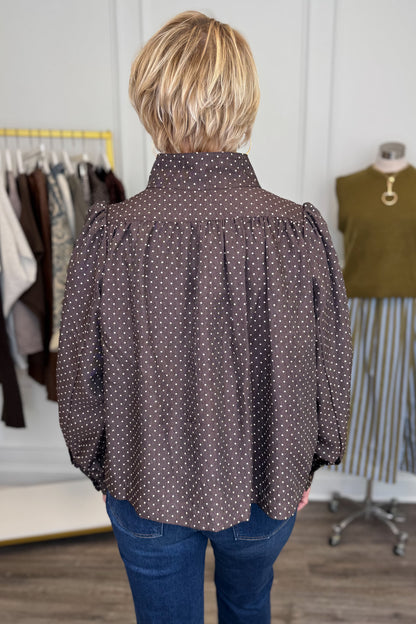 Back view of woman wearing Swagger Boutique’s Polka Dot Button Up Top with jeans with clothing hanging in the background.