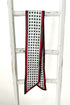 A long white scarf with black polka dots and red trim, draped over a white wooden ladder against a white background.