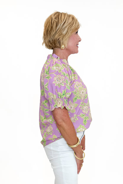 Side view of woman wearing Swagger Boutique’s Purple Floral Short Sleeve Ruffle Top with jeans against white studio background.