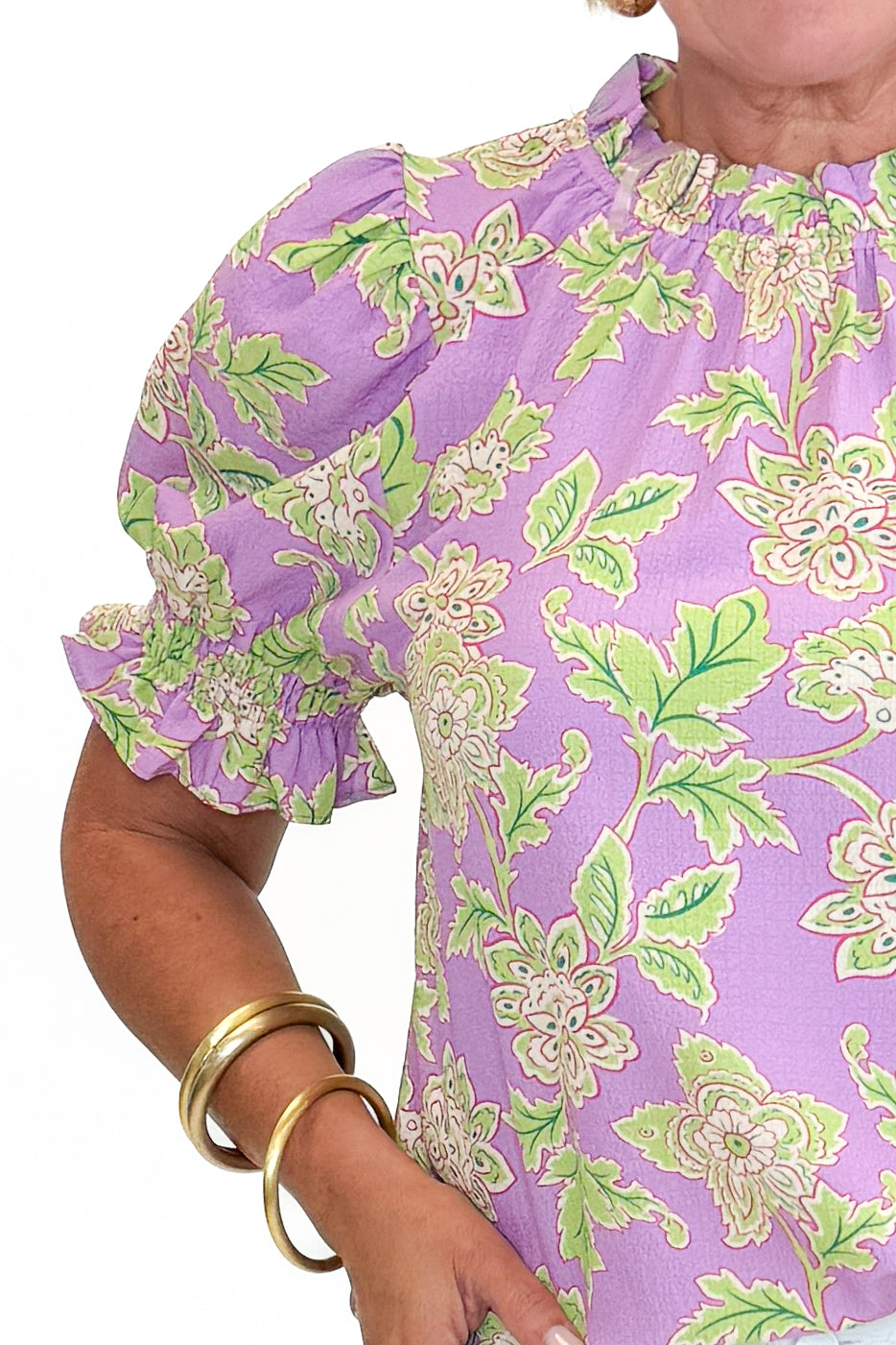 Front detail view of woman wearing Swagger Boutique’s Purple Floral Short Sleeve Ruffle Top with jeans against white studio background.