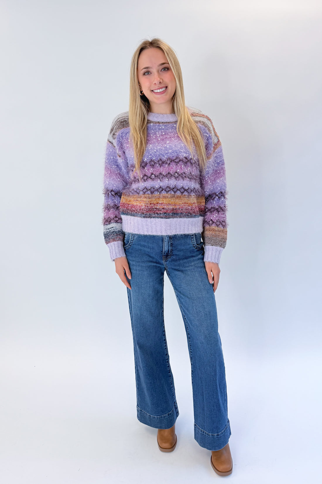 Front view of woman wearing Swagger Boutique’s Purple Printed Eyelash Sweater with jeans against white studio background.