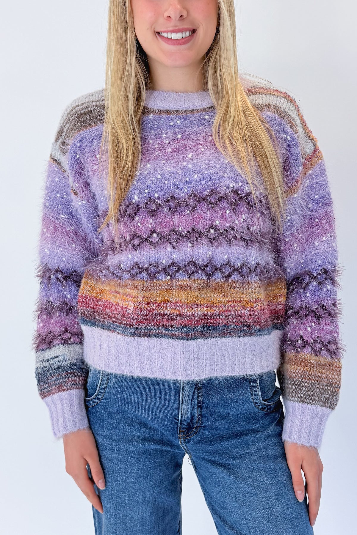 Front detail view of woman wearing Swagger Boutique’s Purple Printed Eyelash Sweater with jeans against white studio background.