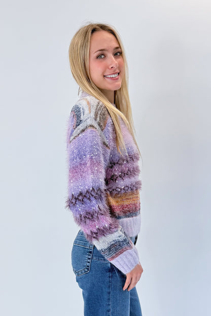 Side view of woman wearing Swagger Boutique’s Purple Printed Eyelash Sweater with jeans against white studio background.