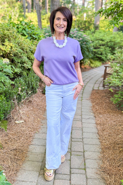Front view of woman wearing Swagger Boutique’s Purple Short Sleeve Banded Top with jeans standing outside. 
