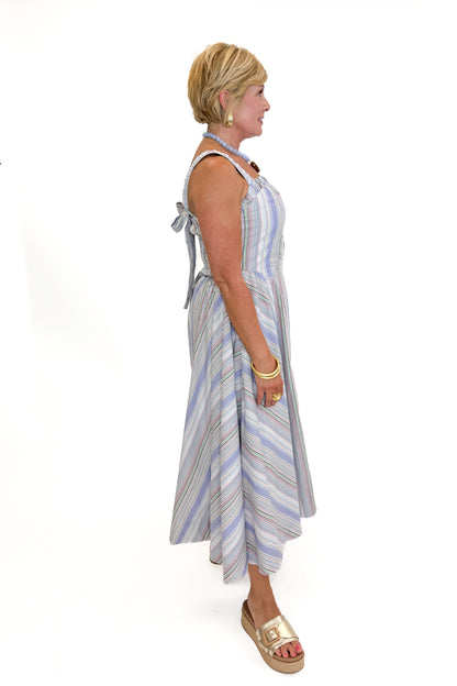 Side view of woman wearing Swagger Boutique’s Purple &amp; Multi Striped Sleeveless Midi Dress with sandals against white studio background.