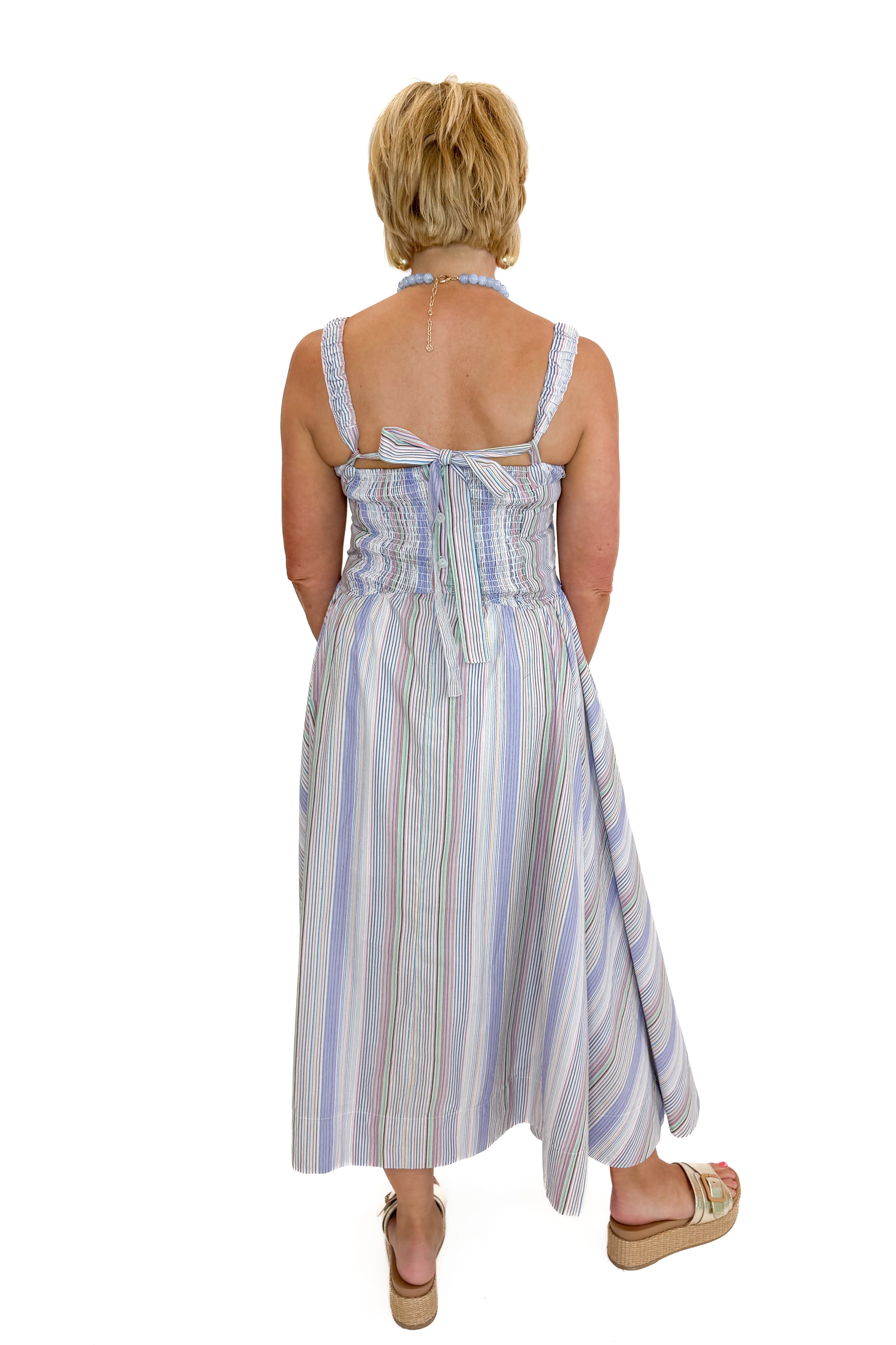 Back view of woman wearing Swagger Boutique’s Purple &amp; Multi Striped Sleeveless Midi Dress with sandals against white studio background.