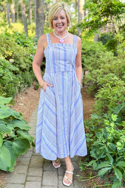Front view of woman wearing Swagger Boutique’s Purple &amp; Multi Striped Sleeveless Midi Dress walking outside at a park.