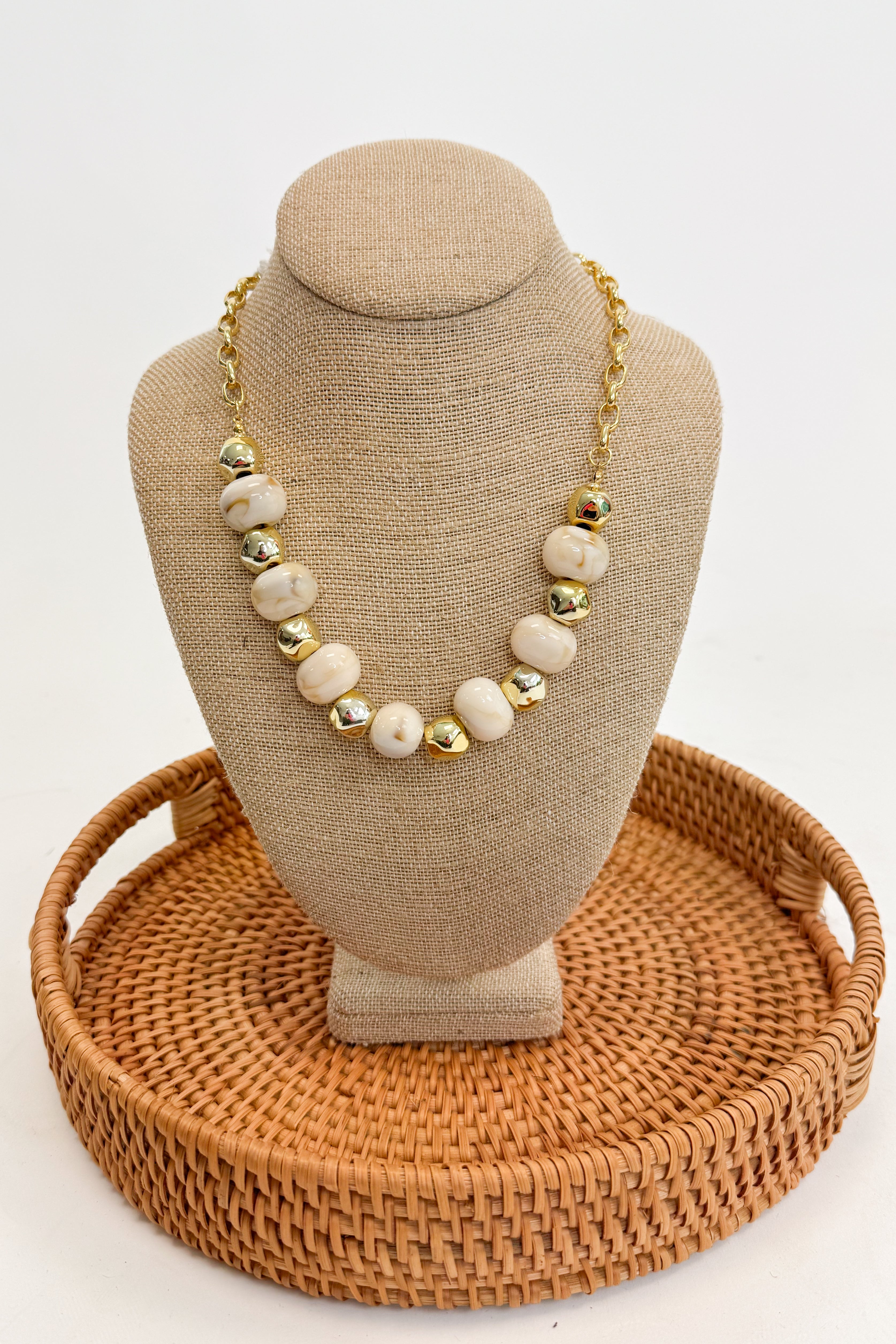 Necklace on a beige bust with a woven brown base against a white background