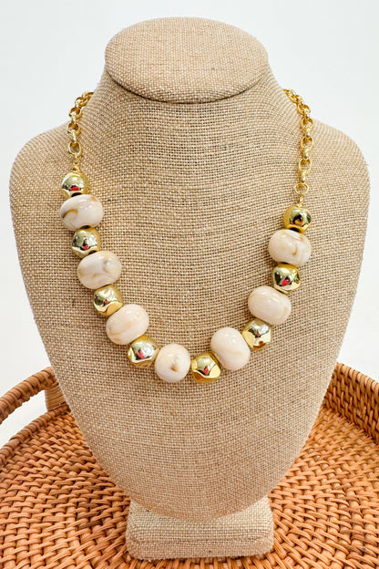 Necklace with white beads and gold accents on a beige bust