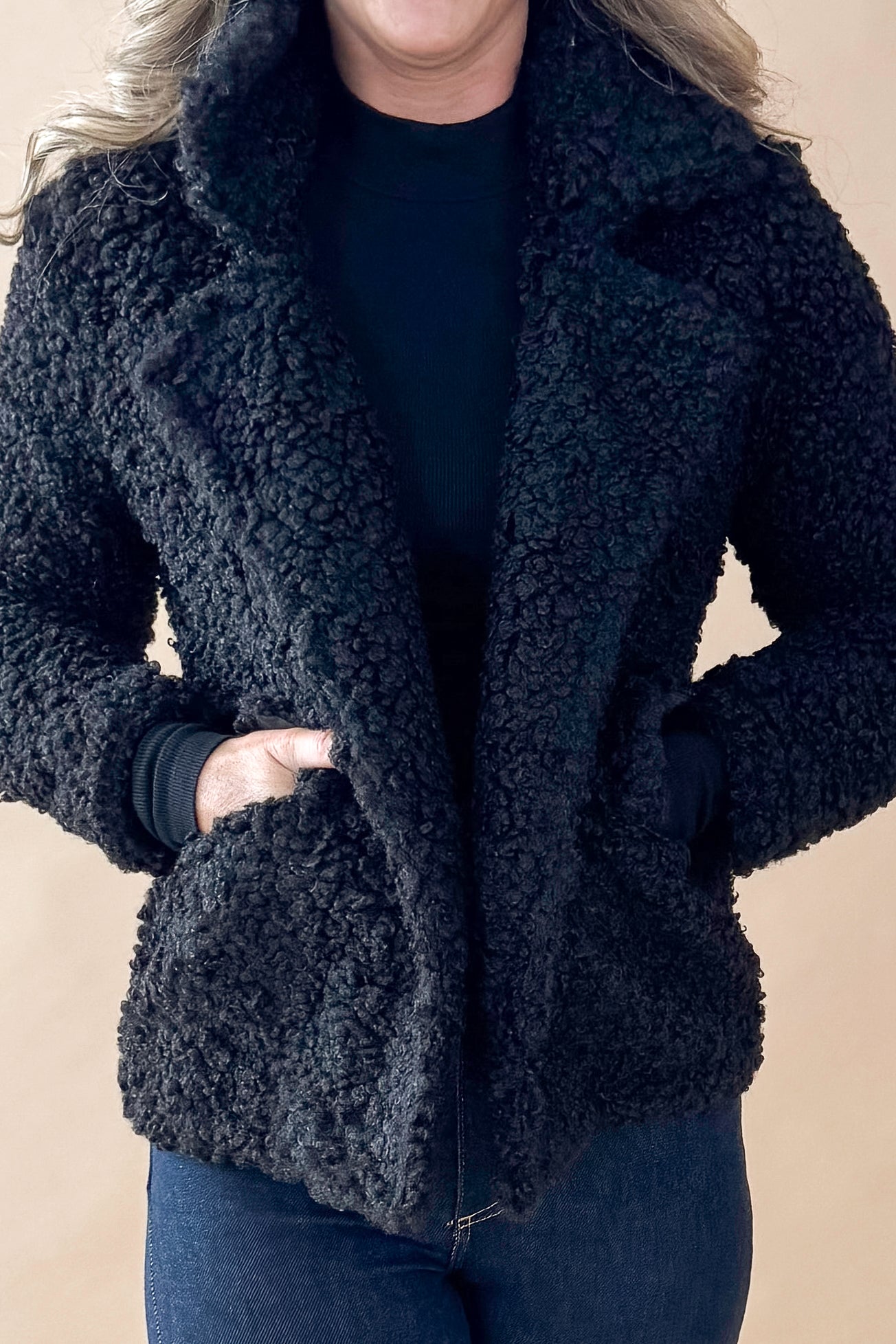 Front detailed view of woman wearing Black Sherpa Coat and jeans against tan studio background.