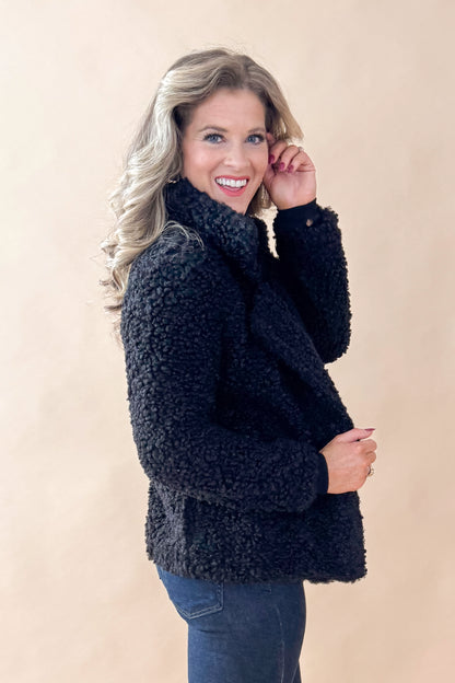 Side view of woman wearing Black Sherpa Coat and jeans against tan studio background.