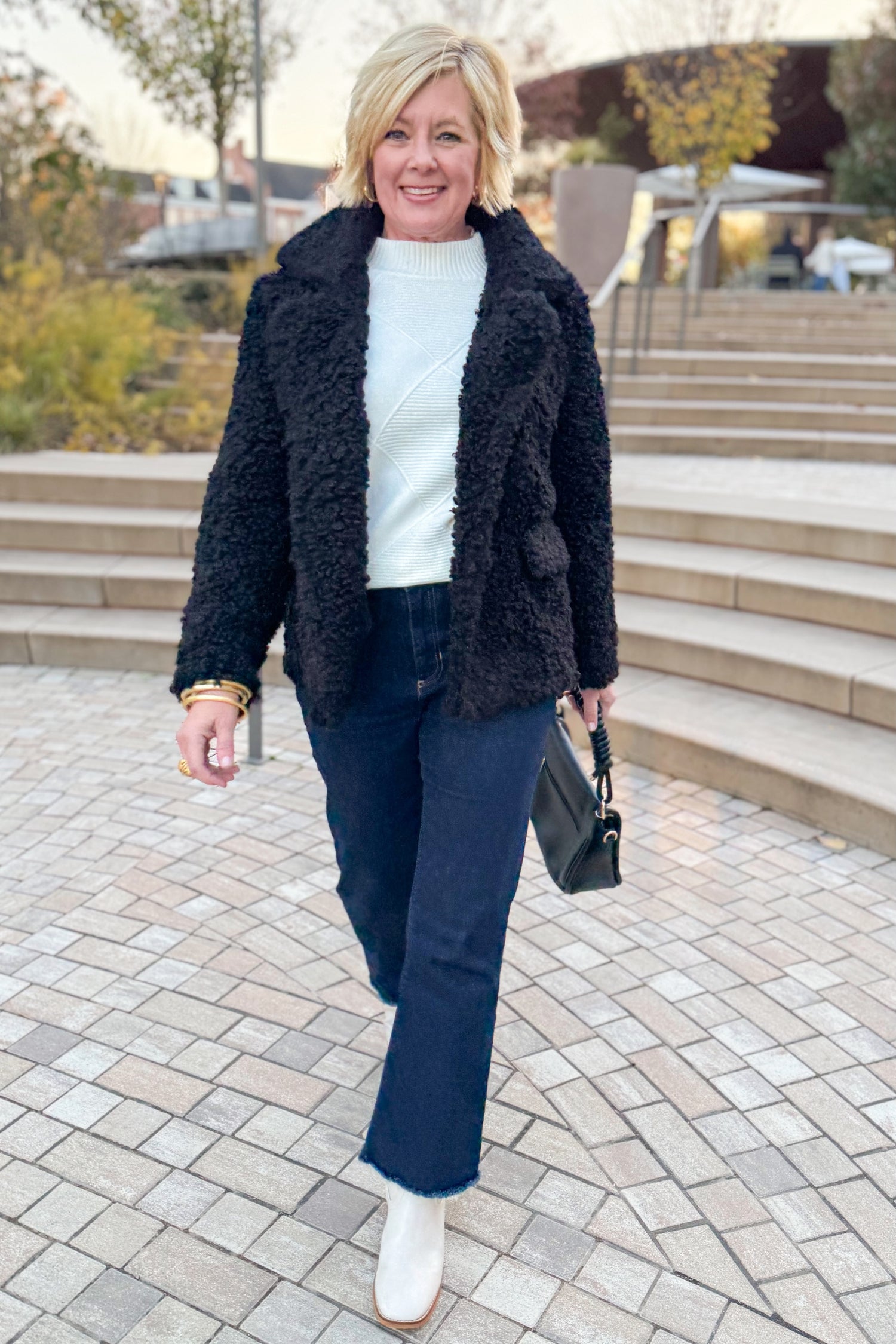 Front view of woman wearing Black Sherpa Coat and jeans outside walking.