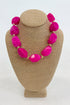 Bold hot pink beaded necklace displayed on a beige jewelry bust, featuring large hot pink beads in a chunky statement style.