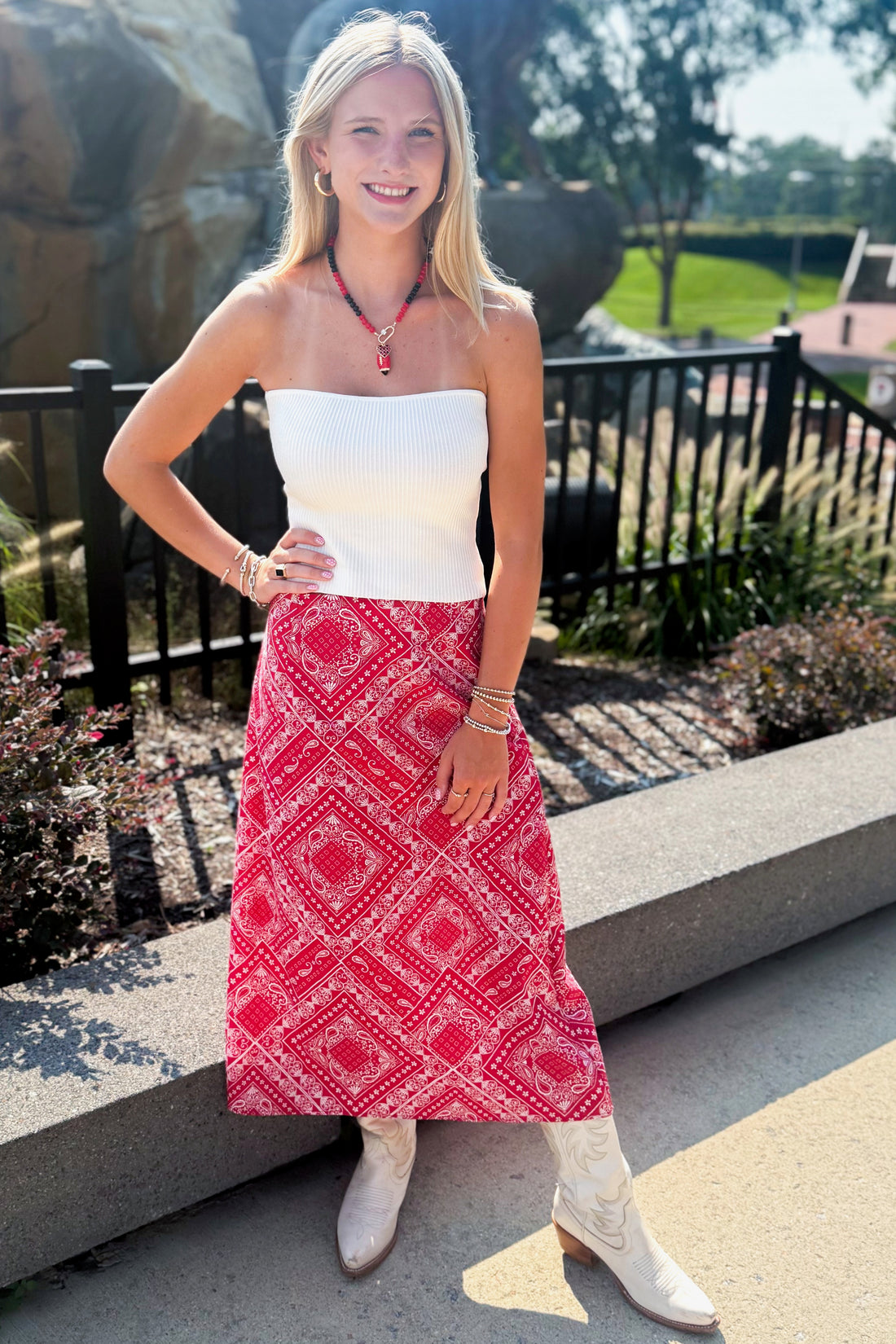 Front view of woman wearing Swagger Boutique’s Red Bandana Print Midi Skirt with white top standing outside at a park.