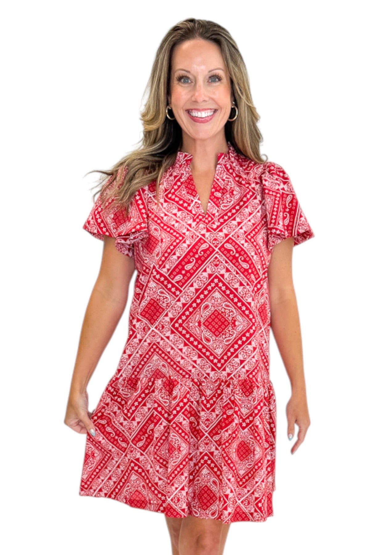 Front view of woman wearing Swagger Boutique’s Red Bandana Print Mini Dress with sandals against white studio background.