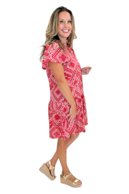 Side view of woman wearing Swagger Boutique’s Red Bandana Print Mini Dress with sandals against white studio background.