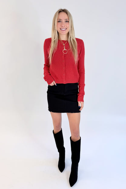 Front view of woman wearing Swagger Boutique’s Red Button Up Cardigan with Black Denim Mini Skirt by Just Black Denim against white studio background.