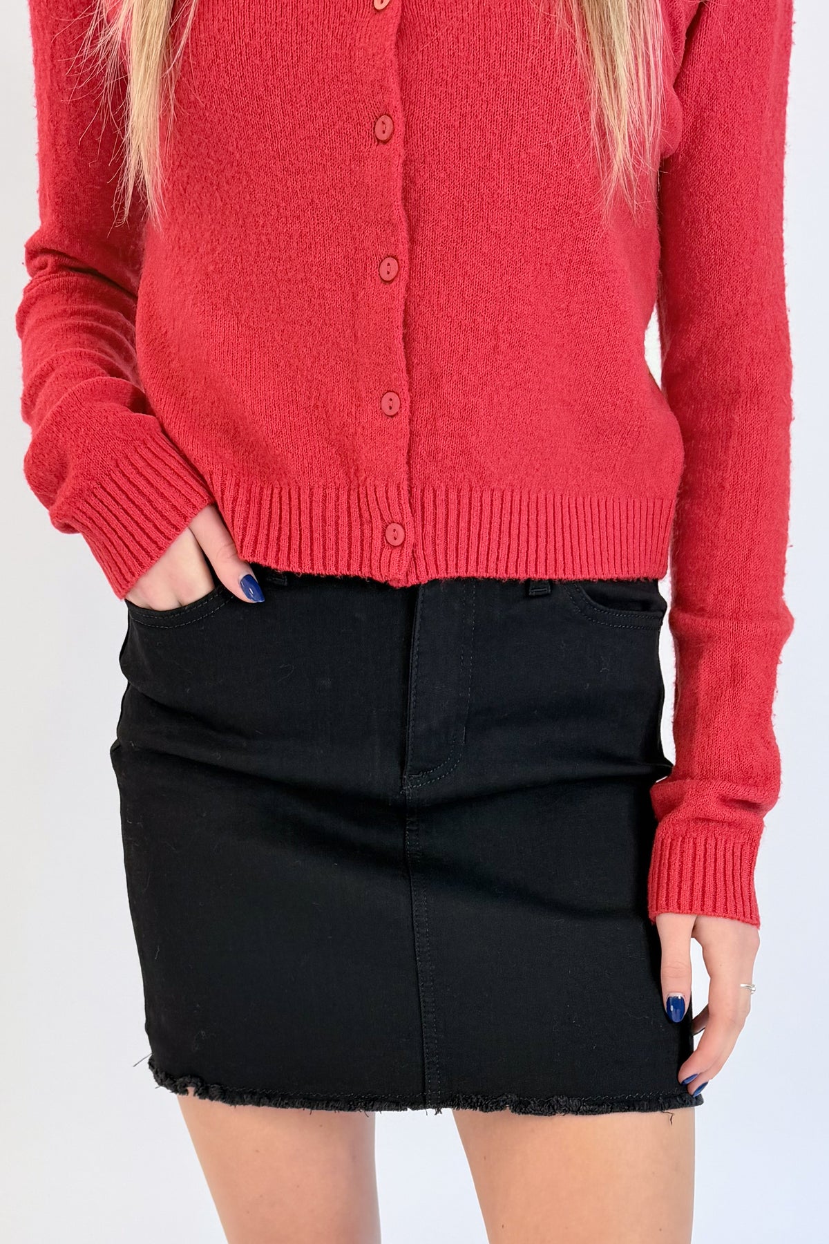 Front detail view of woman wearing Swagger Boutique’s Red Button Up Cardigan with Black Denim Mini Skirt by Just Black Denim against white studio background.