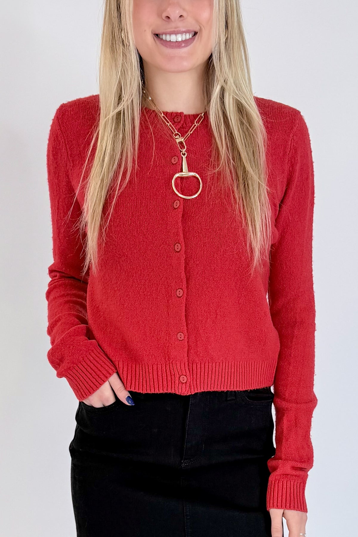 Front detail view of woman wearing Swagger Boutique’s Red Button Up Cardigan with Black Denim Mini Skirt by Just Black Denim against white studio background.