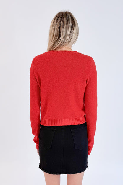 Back view of woman wearing Swagger Boutique’s Red Button Up Cardigan with Black Denim Mini Skirt by Just Black Denim against white studio background.