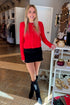 Front view of woman wearing Swagger Boutique’s Red Button Up Cardigan with Black Denim Mini Skirt by Just Black Denim standing at the store.