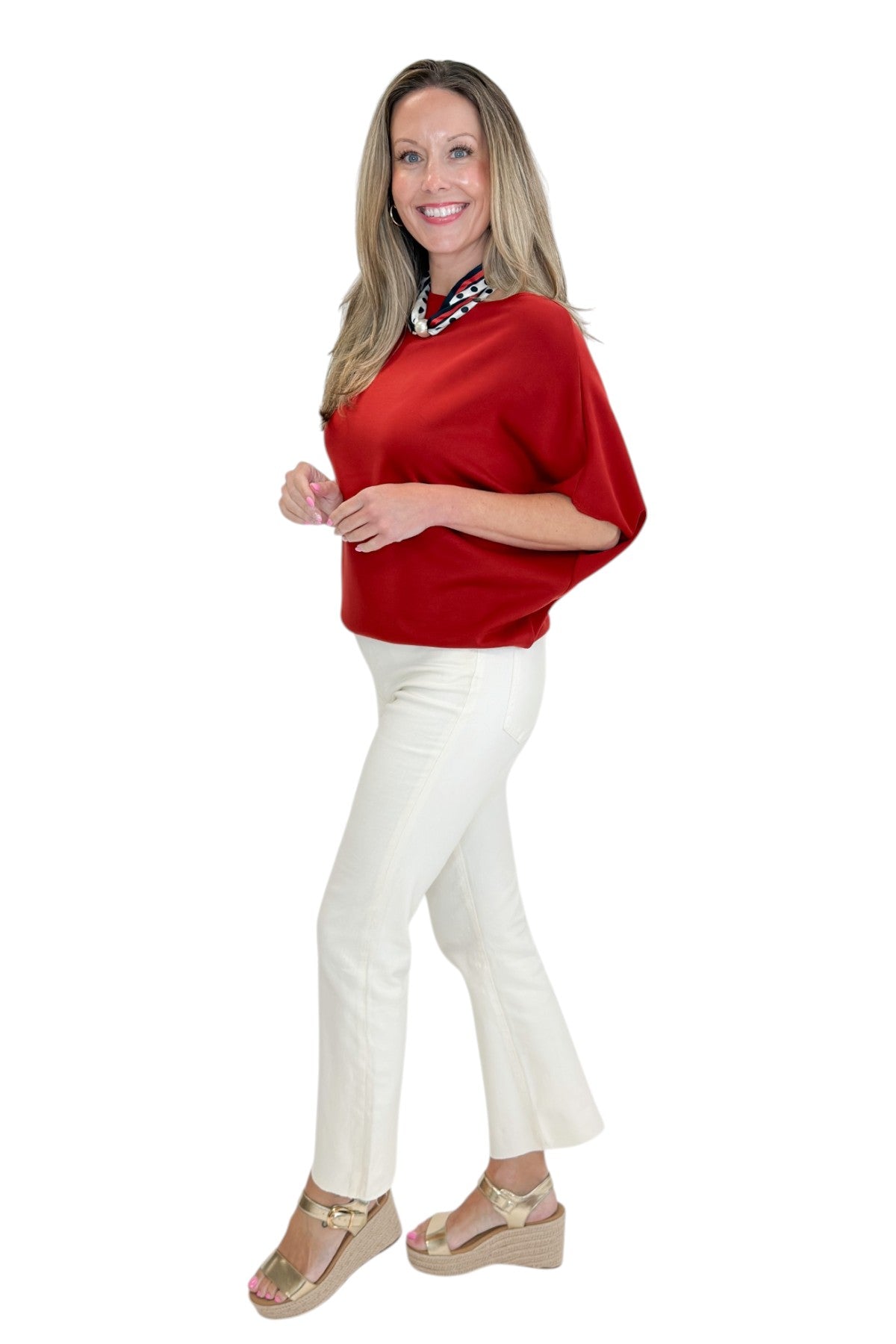 Side view of woman wearing Swagger Boutique’s Red Dolman Sleeve Top with jeans against white studio background.