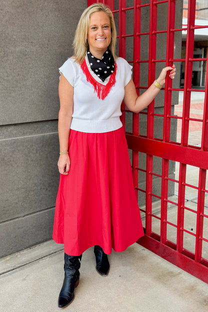 Front view of woman wearing Swagger Boutique’s Red Elastic Waist Midi Skirt with boots standing outside at a stadium gate.