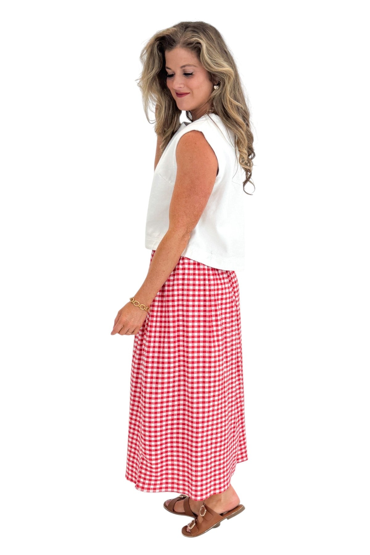 Side view of woman wearing Swagger Boutique’s Red Gingham Flowy Midi Skirt with White Denim Tank against white studio background.