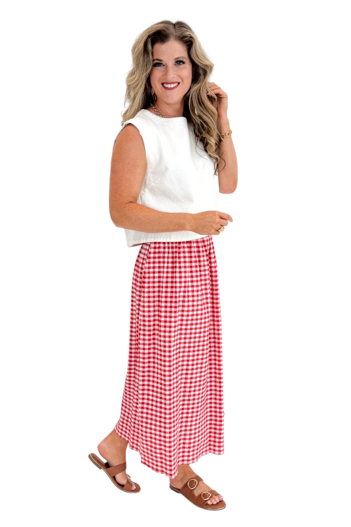Side view of woman wearing Swagger Boutique’s Red Gingham Flowy Midi Skirt with White Denim Tank against white studio background.