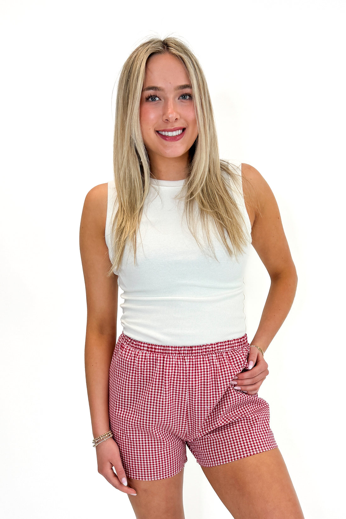 Front view of woman wearing Swagger Boutique’s Red Gingham Shorts with Off White Round Hem Ribbed Tank against white studio background.
