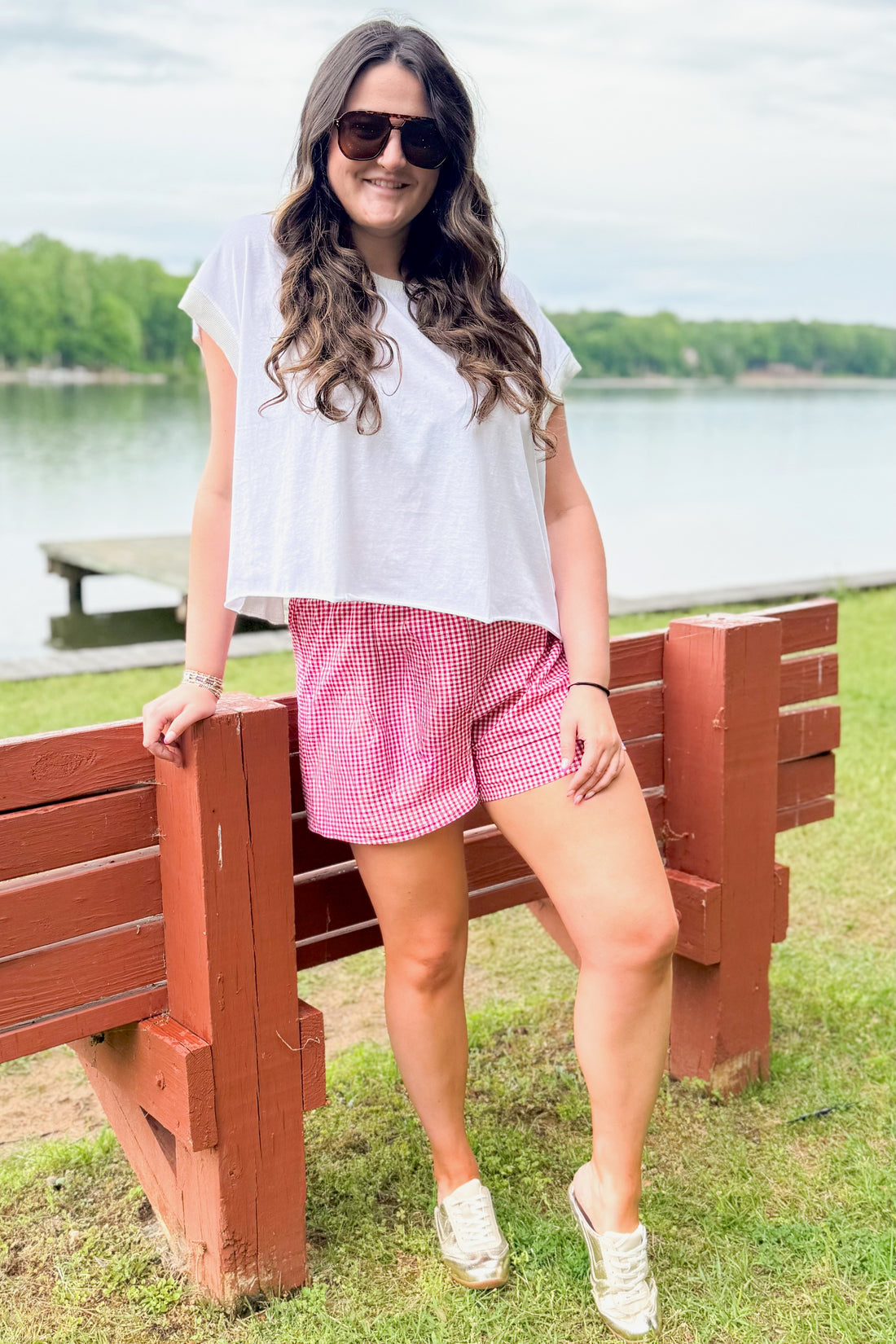 Front view of woman wearing Swagger Boutique’s Red Gingham Shorts with White Open Back top outside at the lake.