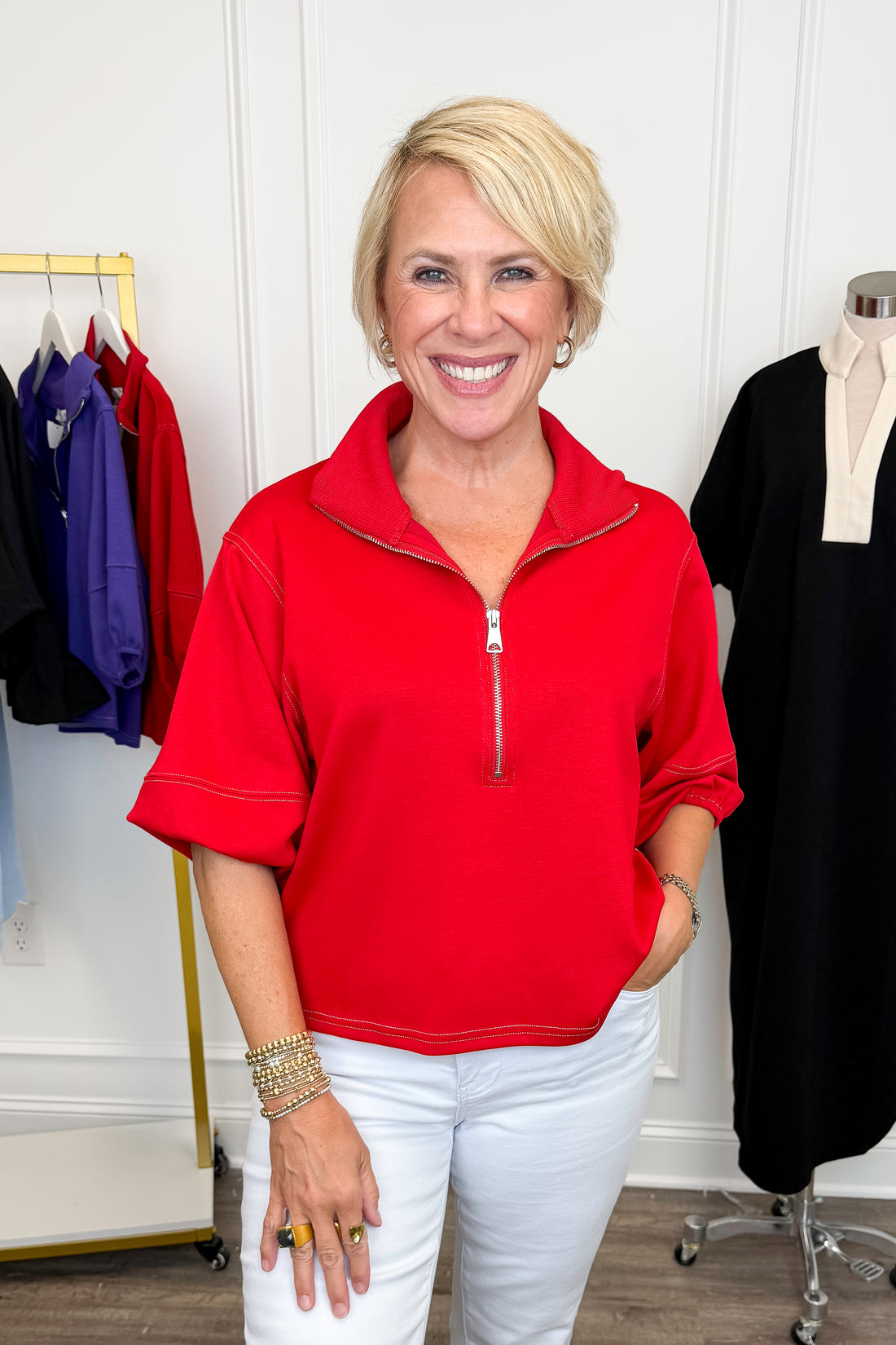 Front view of woman wearing Swagger Boutique’s Red Puff Sleeve 1_4 Zip Sweatshirt with jeans with clothing hanging in the background.