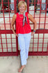 Front view of woman wearing Swagger Boutique’s Red Ruffle Tank with jeans standing by a stadium gate.