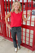 Front view of woman wearing Swagger Boutique’s Red Smocked Trim Tank with Black & White Polka Dot Crop Flare Jeans by Just Black Denim standing at a red gate.