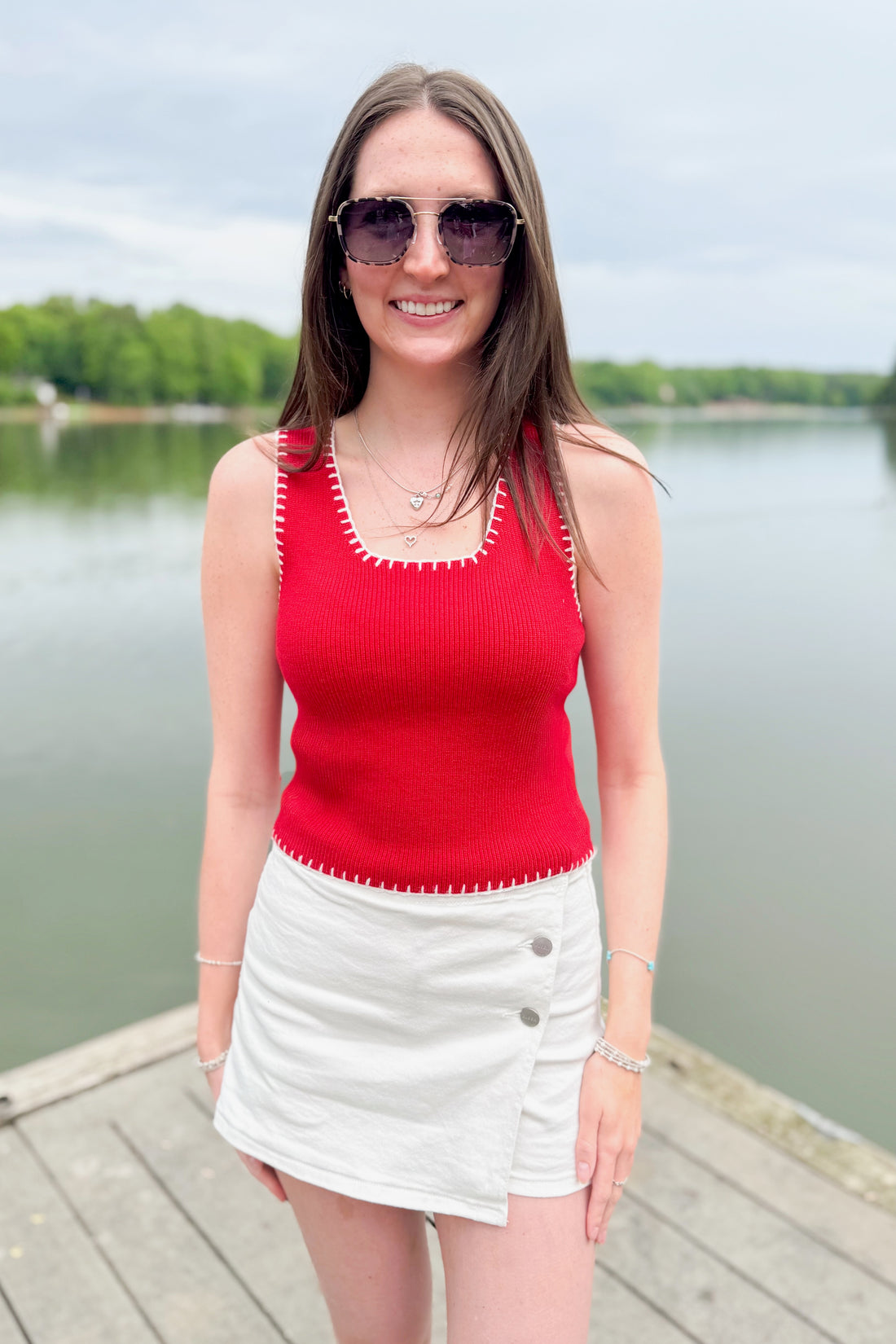 Front view of woman wearing Swagger Boutique’s Red Stitch Detail Sweater Tank with White High Rise Button Down Denim Skort by Risen outside at the lake.
