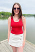 Front view of woman wearing Swagger Boutique’s Red Stitch Detail Sweater Tank with White High Rise Button Down Denim Skort by Risen outside at the lake.