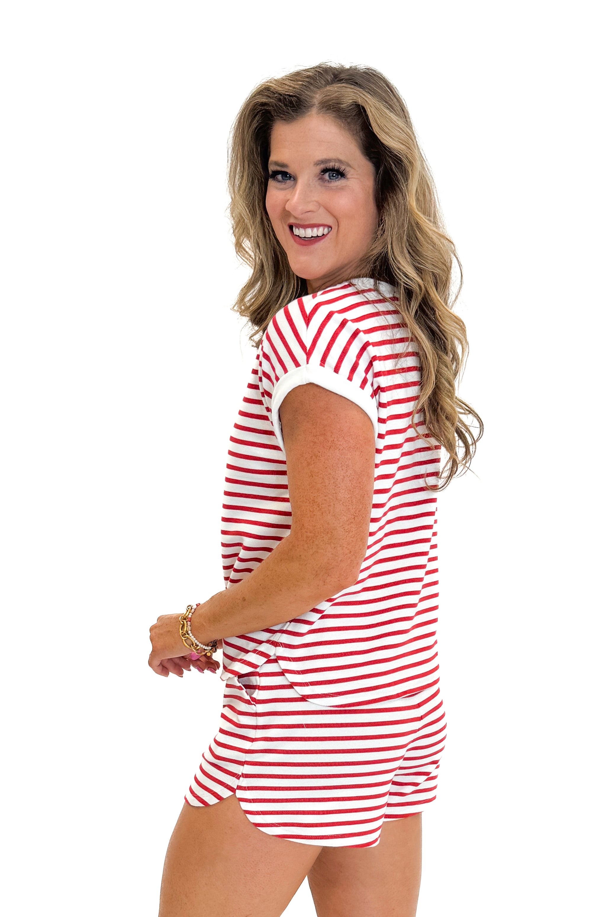Side view of woman wearing Swagger Boutique’s Red Striped Relaxed Fit Top with red striped shorts against white studio background.