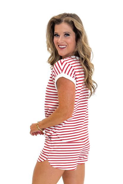 Side view of woman wearing Swagger Boutique’s Red Striped Relaxed Fit Top with red striped shorts against white studio background.
