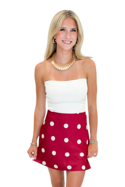 Front view of woman wearing Swagger Boutique’s white top with Red &amp; Cream Polka Dot Satin Mini Skirt against white studio background.