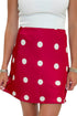 Front detail view of woman wearing Swagger Boutique’s white top with Red & Cream Polka Dot Satin Mini Skirt against white studio background.