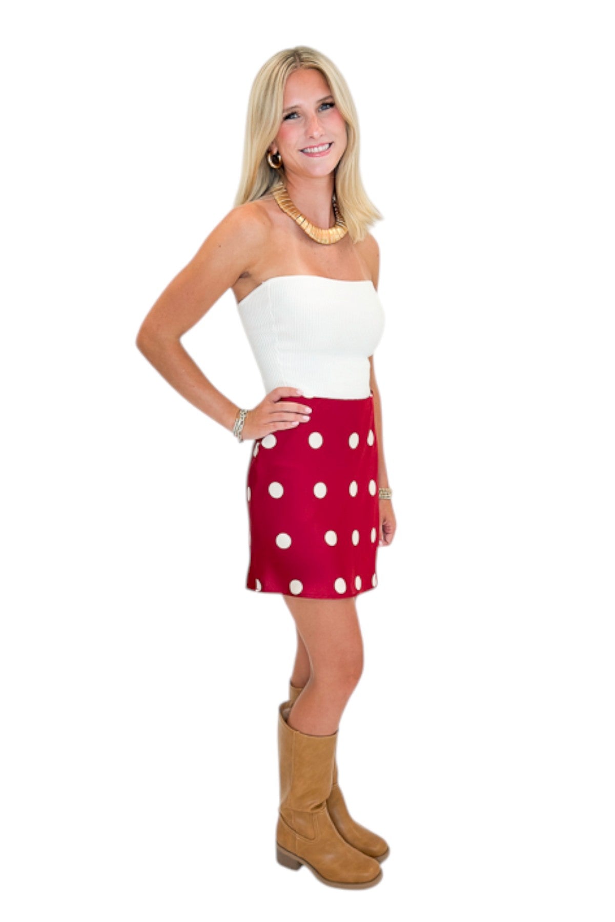 Side view of woman wearing Swagger Boutique’s white top with Red &amp; Cream Polka Dot Satin Mini Skirt against white studio background.