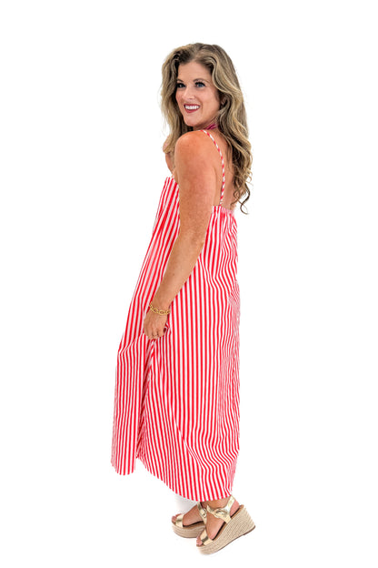 Side view of woman wearing Swagger Boutique’s Red &amp; Pink Striped Maxi Dress with sandals against white studio background.