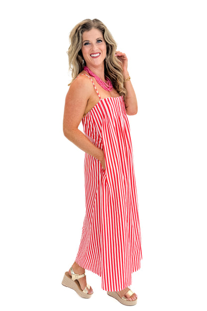 Side view of woman wearing Swagger Boutique’s Red &amp; Pink Striped Maxi Dress with sandals against white studio background.