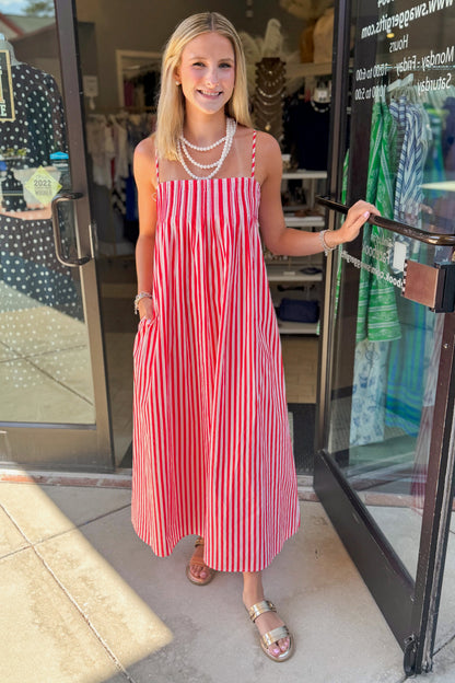 Front view of woman wearing Swagger Boutique’s Red &amp; Pink Striped Maxi Dress with sandals standing outside the store.