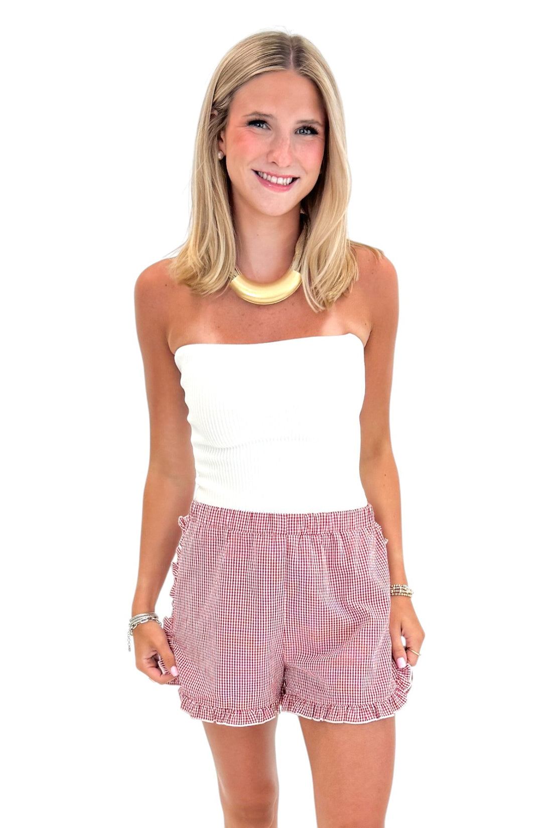 Front view of woman wearing Swagger Boutique’s Red &amp; White Gingham Ruffle Shorts with white top against white studio background.