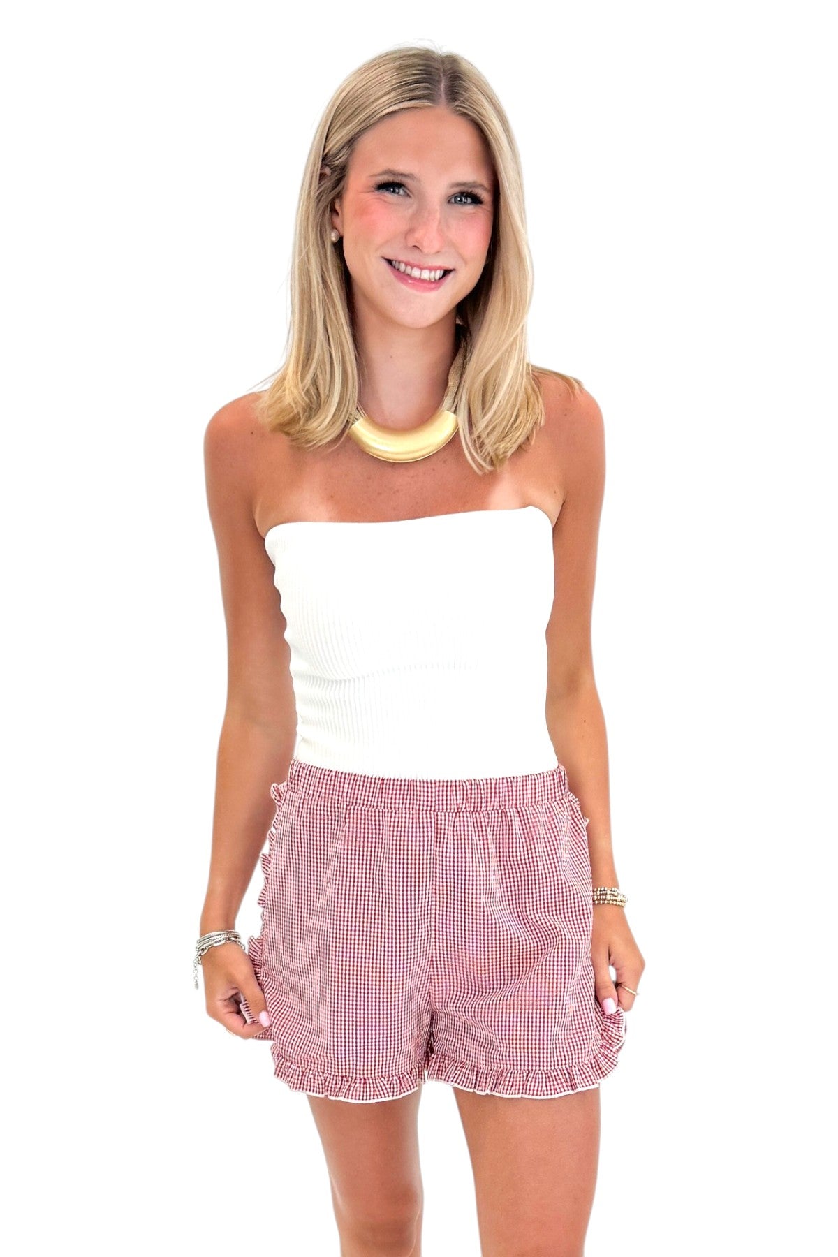Front view of woman wearing Swagger Boutique’s Red &amp; White Gingham Ruffle Shorts with white top against white studio background.