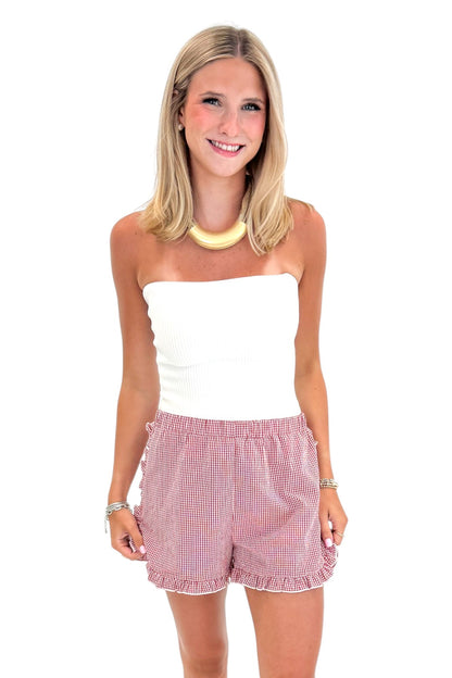 Front view of woman wearing Swagger Boutique’s Red &amp; White Gingham Ruffle Shorts with white top against white studio background.