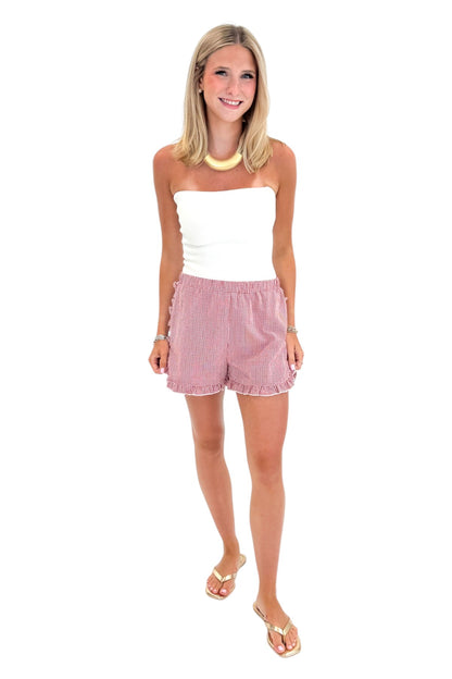 Front view of woman wearing Swagger Boutique’s Red &amp; White Gingham Ruffle Shorts with white top against white studio background.